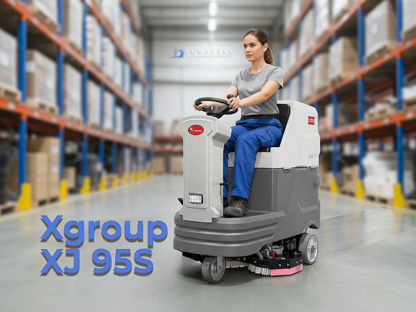 Поломоечная машина XGroup XJ95S с местом для оператора работает в крупном складском комплексе с высокими стеллажами. Машина проезжает по широким проходам, две щетки вращаются, оставляя за собой чистый блестящий пол. Оператор сидит в удобном кресле, управл